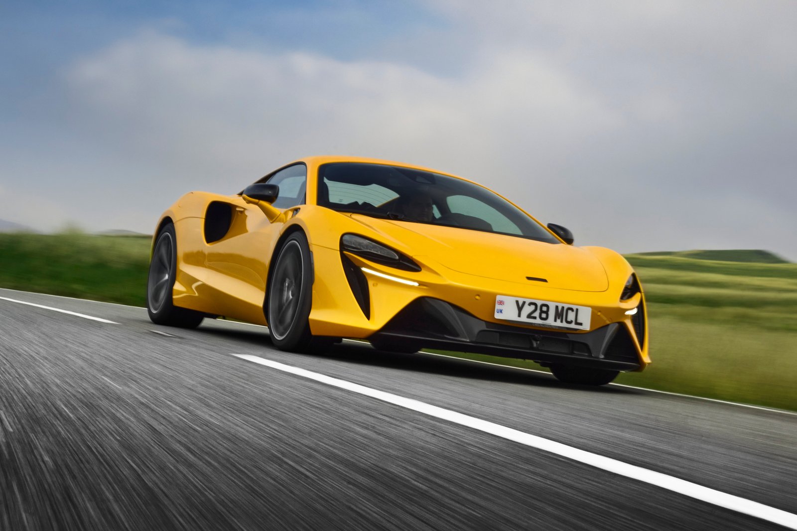 Yellow McLaren Artura driving on a rural road