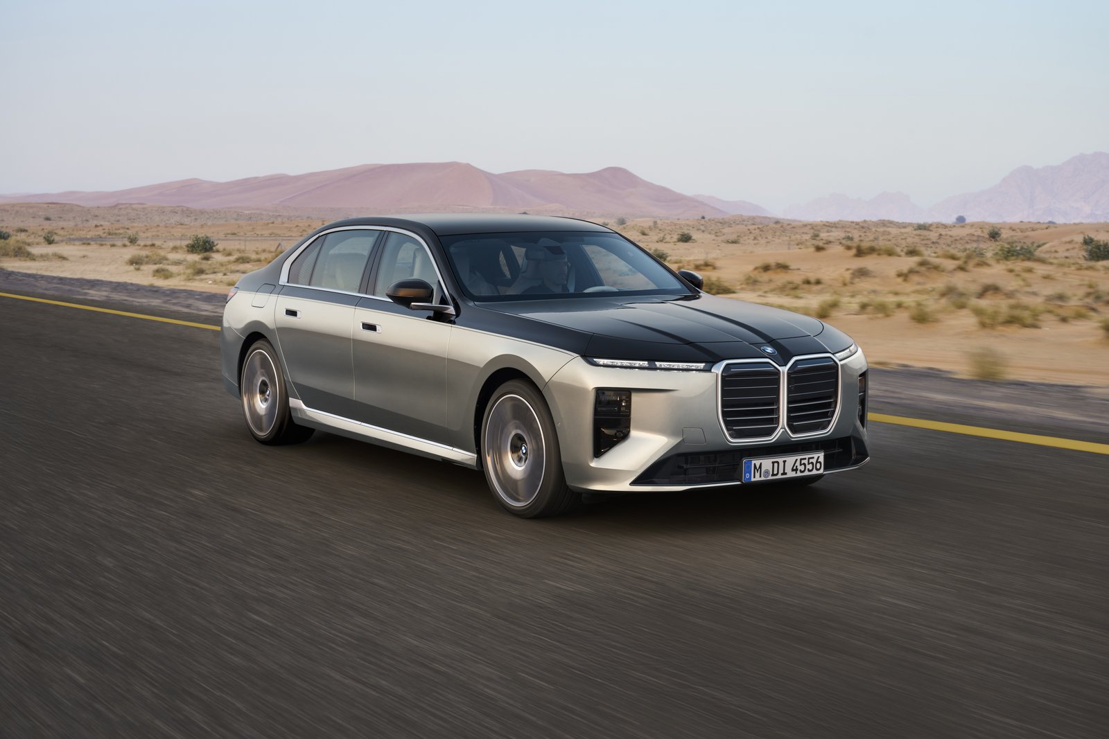Two-tone BMW 7 Series sedan driving on a desert highway