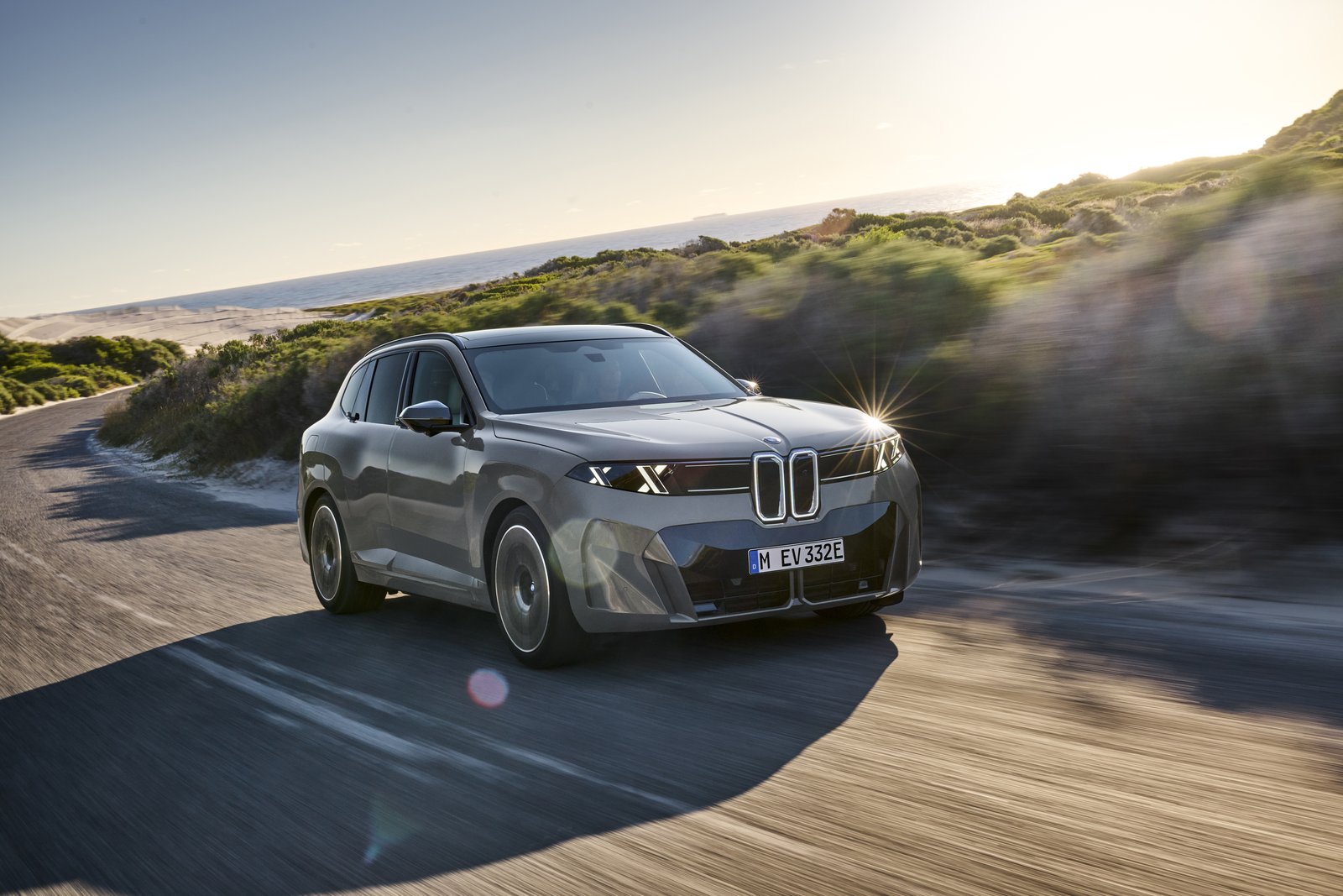 Gray BMW iX5 60 xDrive electric SUV driving on a coastal road