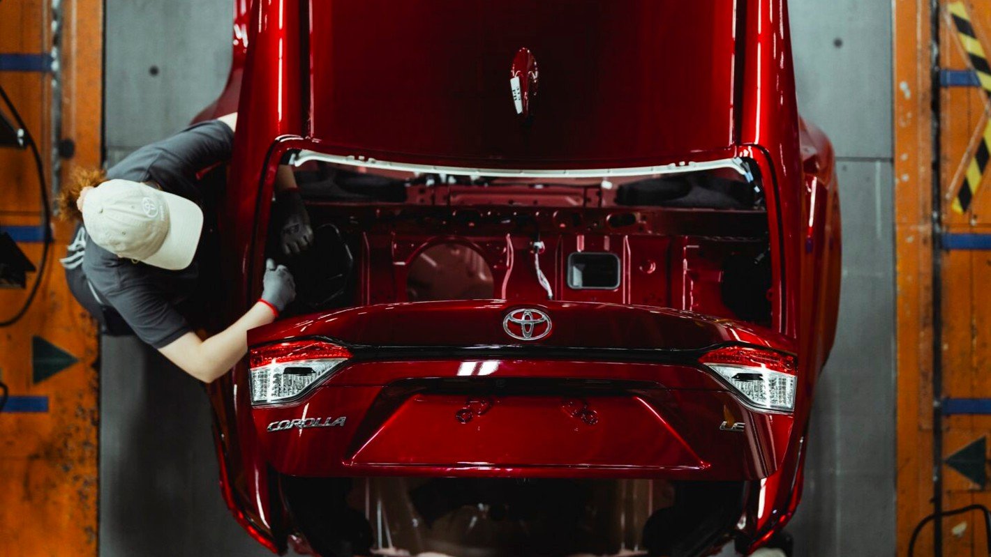 Worker fitting parts inside the trunk of a red Toyota Corolla LE