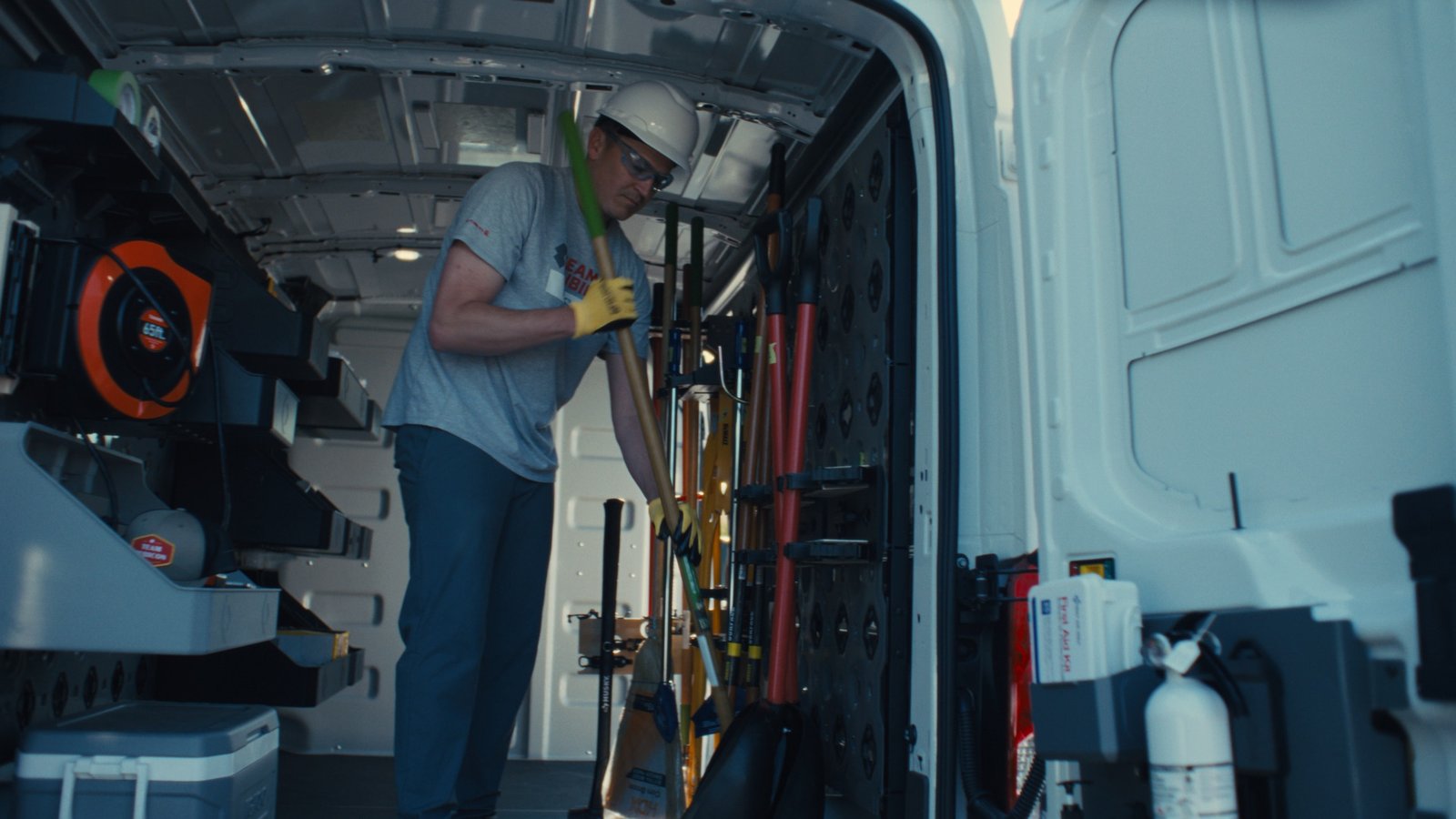 Volunteer loading long-handled tools into GRIDRACK mounts inside the Transit