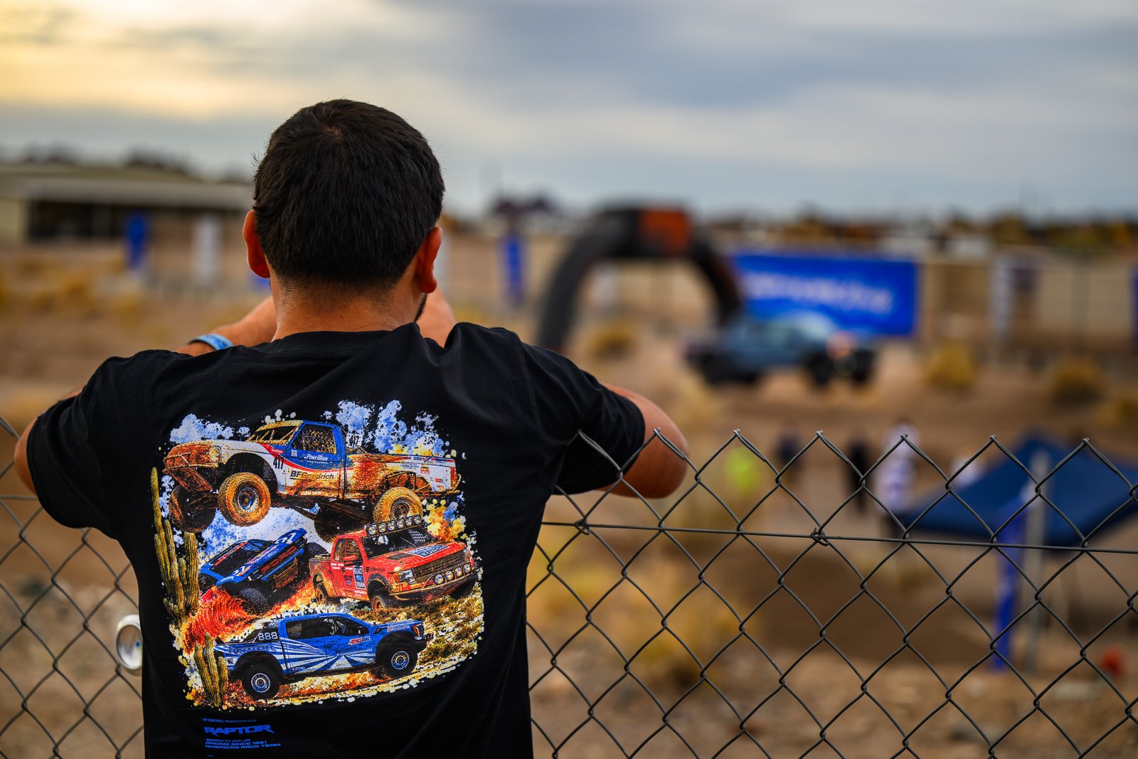 Spectator at a chain-link fence wearing a Ford Racing Raptor heritage T-shirt