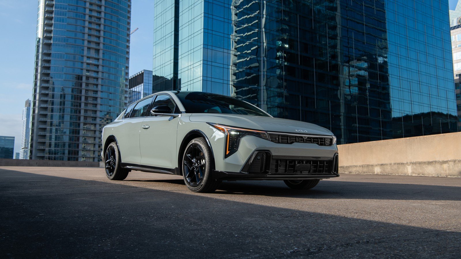 2027 Kia K4 sedan front three-quarter view in front of glass towers