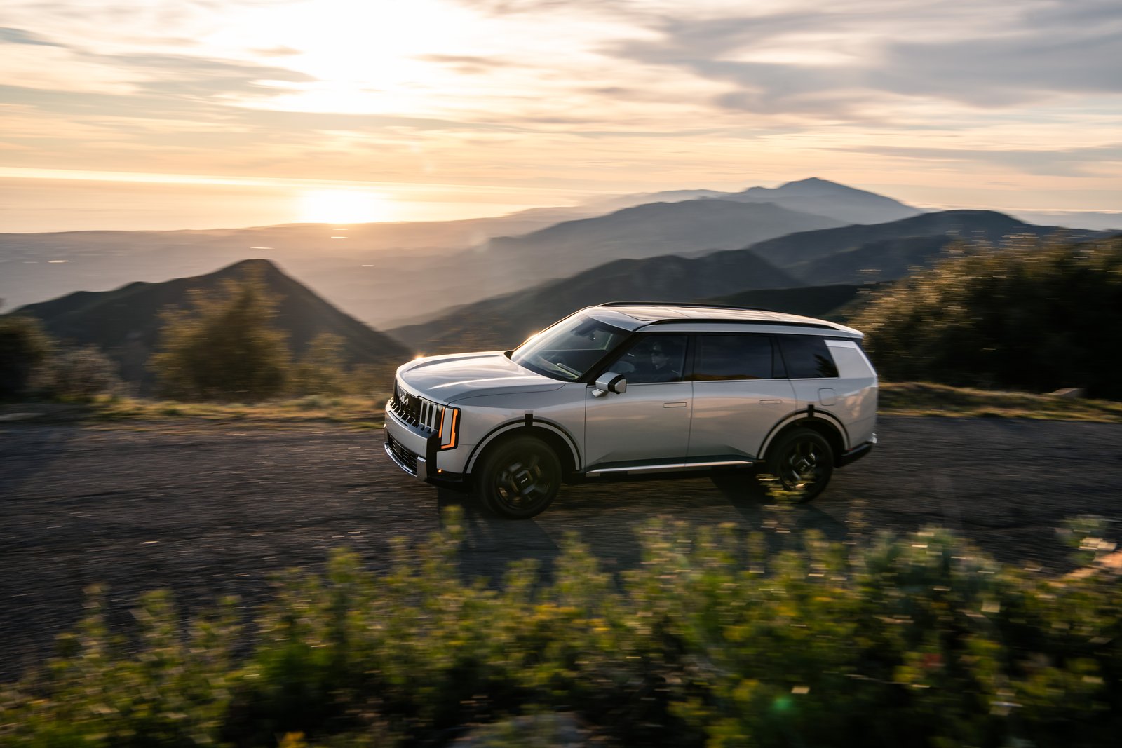 Side view of a silver 2027 Kia Telluride Hybrid driving on a ridge road