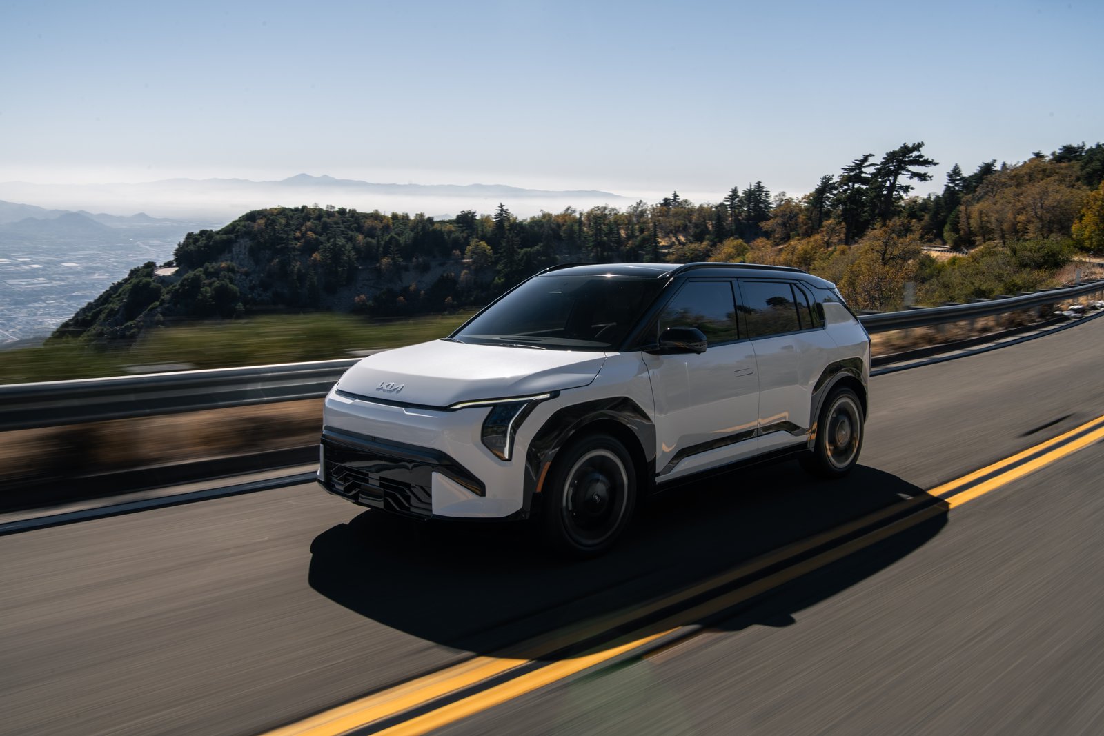White 2027 Kia EV3 driving on a mountain road, front three-quarter view