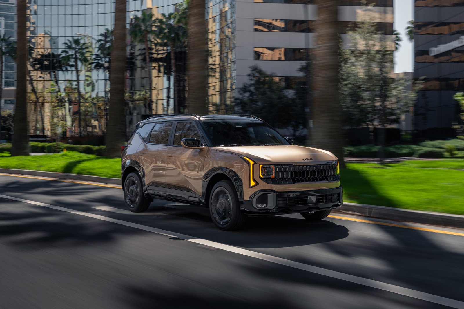 Tan 2027 Kia Seltos driving on a palm-lined city street