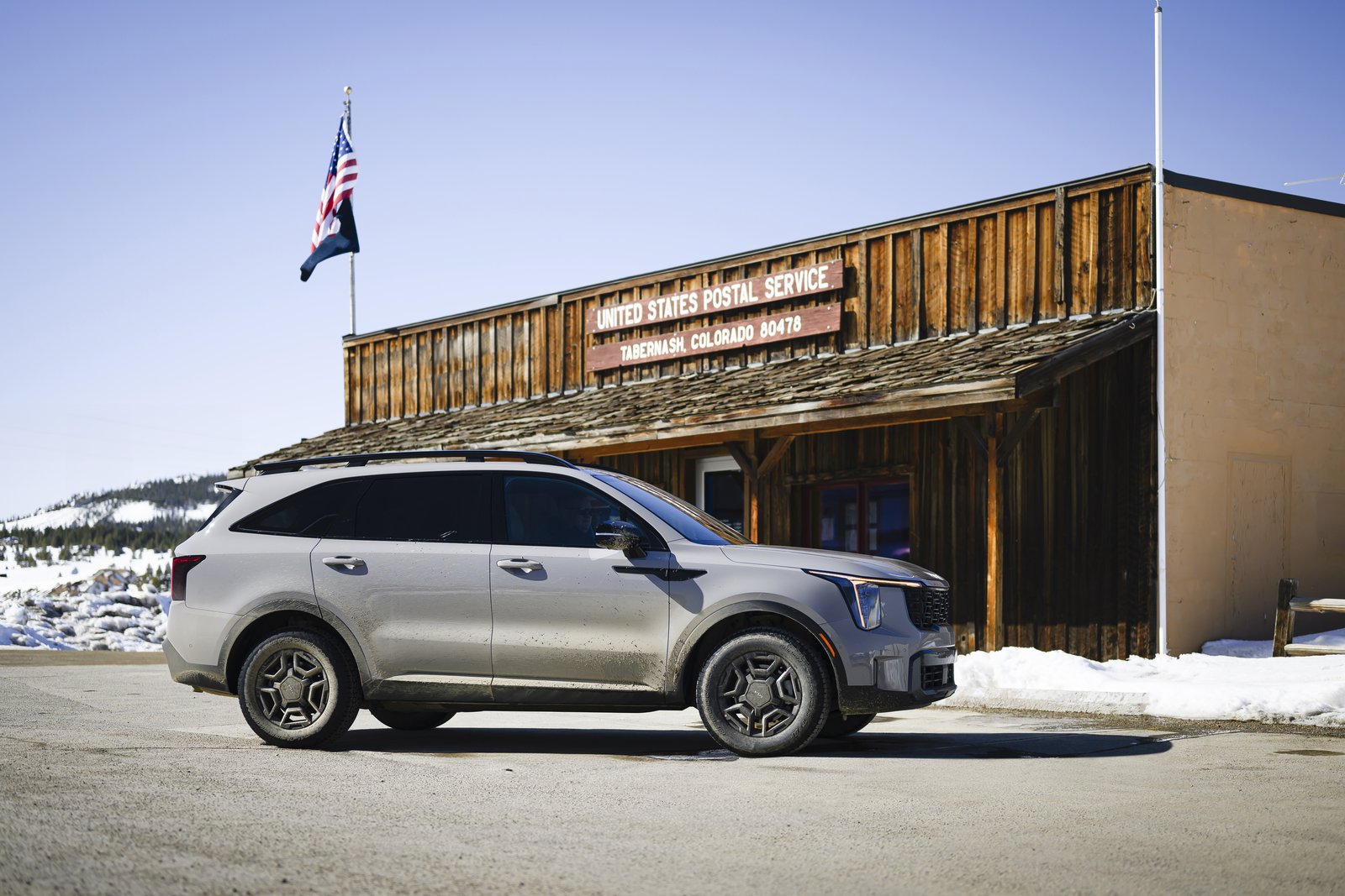 2027 Kia Sorento side profile in front of a wooden building