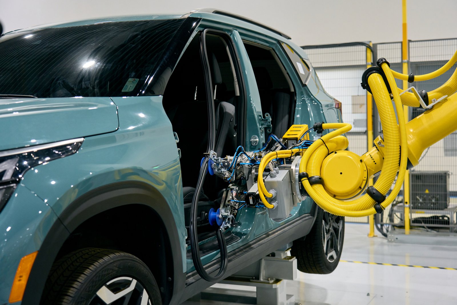 Yellow robot arm fits a door seal on a teal Kia SUV