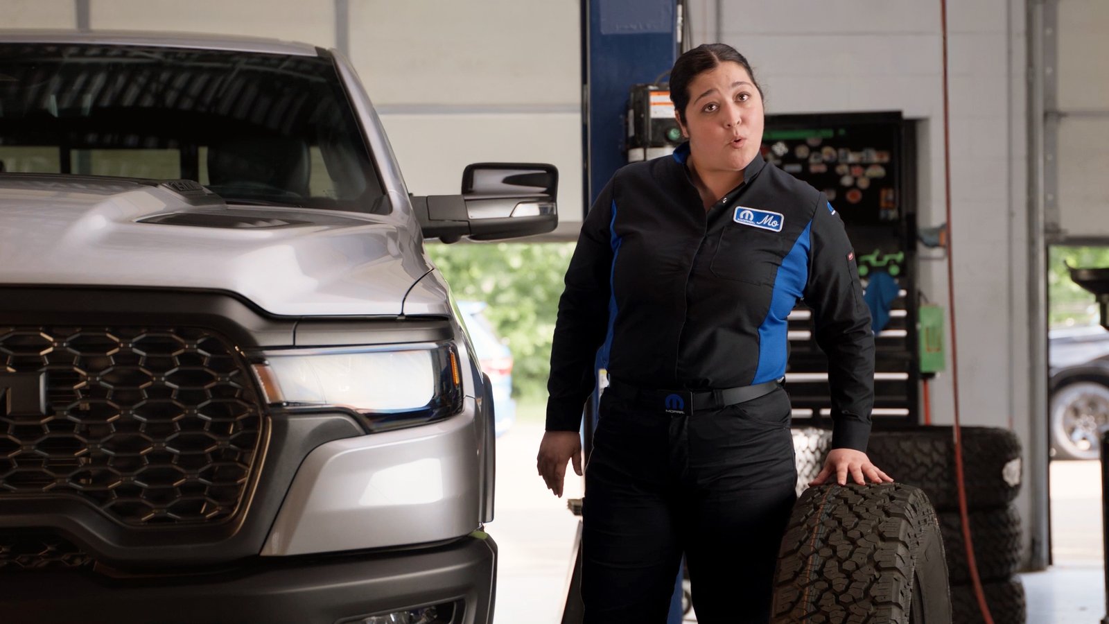 Mopar technician with an all-terrain tire beside a silver Ram 1500 pickup