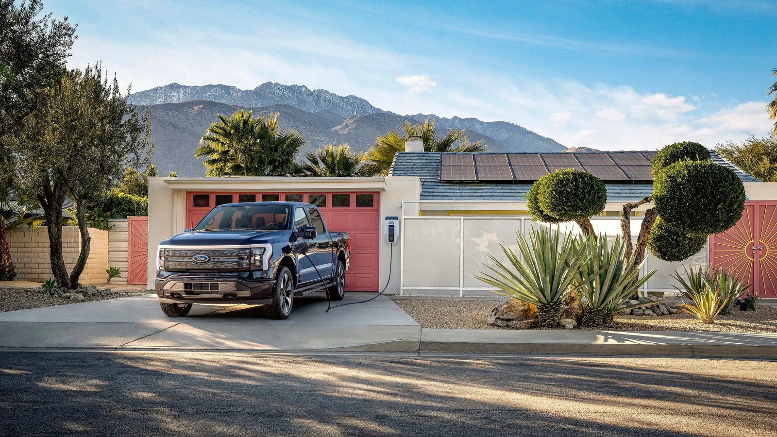 Ford F-150 Lightning plugged into a Ford Charge Station Pro outside a house with solar panels