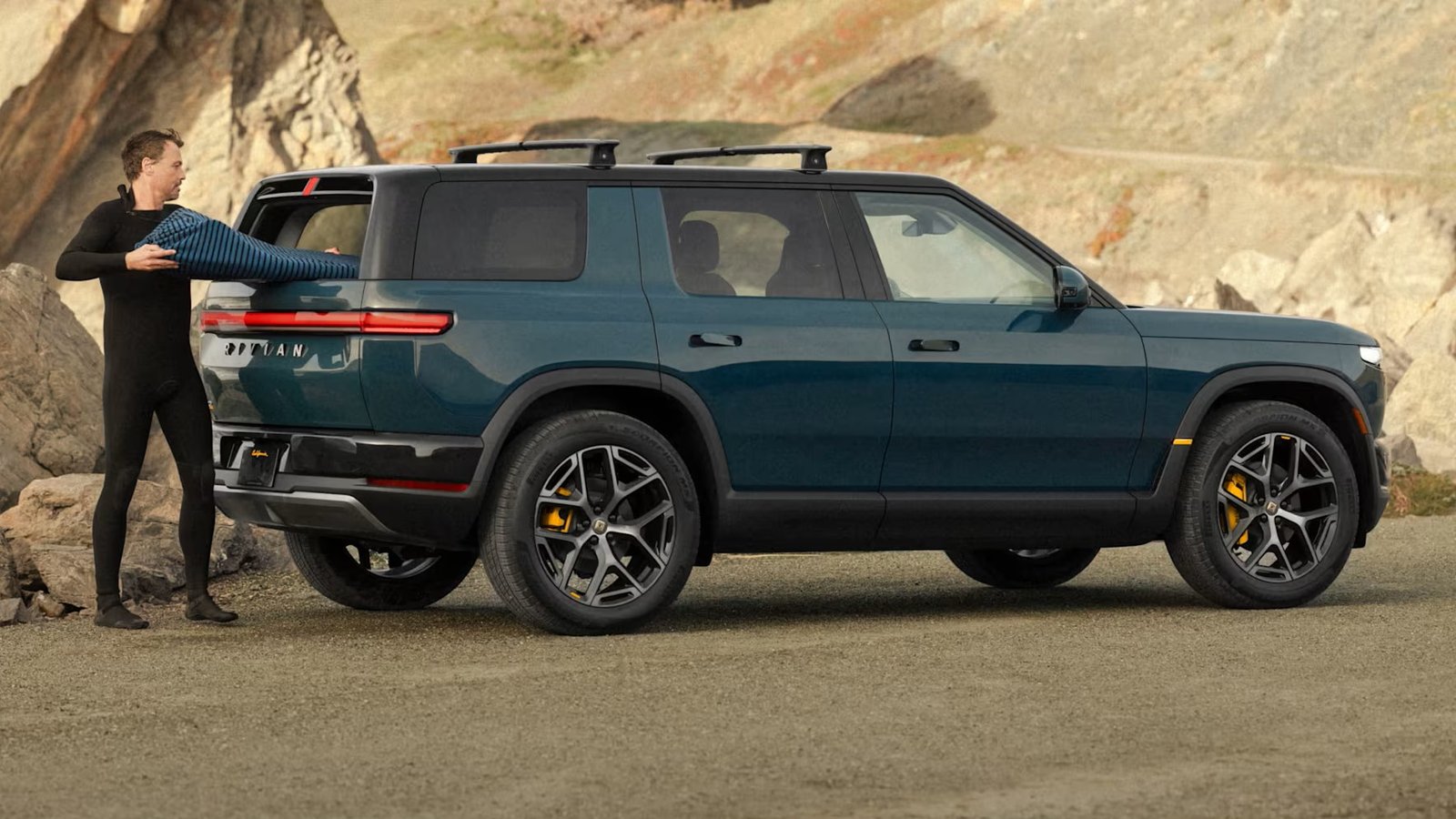 Blue Rivian R2 Performance parked by a rocky beach, side view