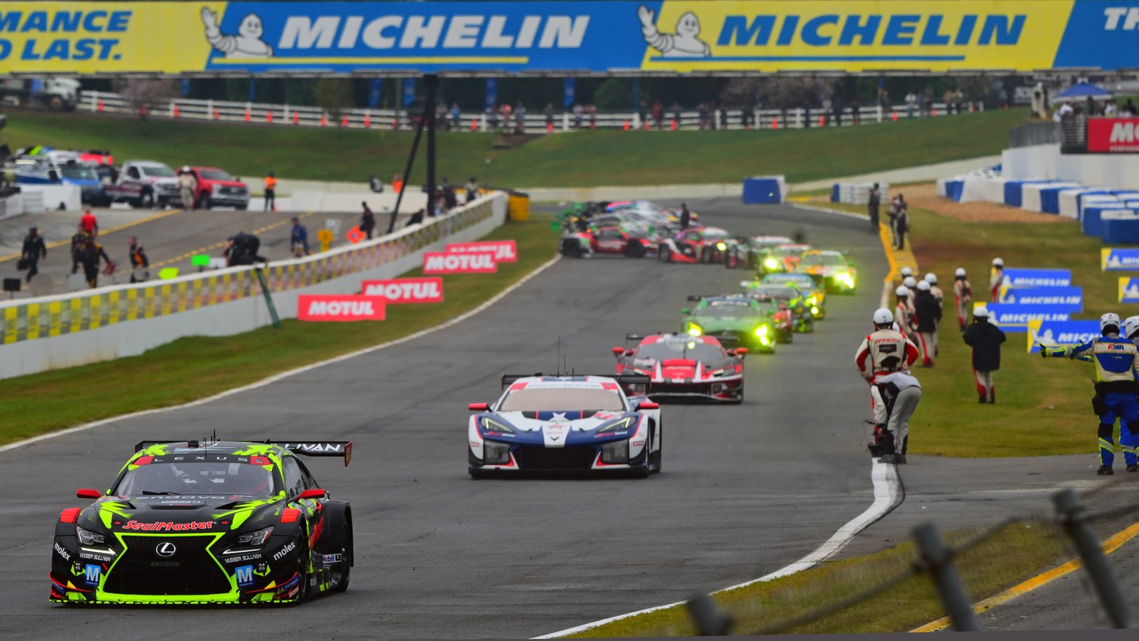 Lexus RC F GT3 leading a line of GT cars past track marshals