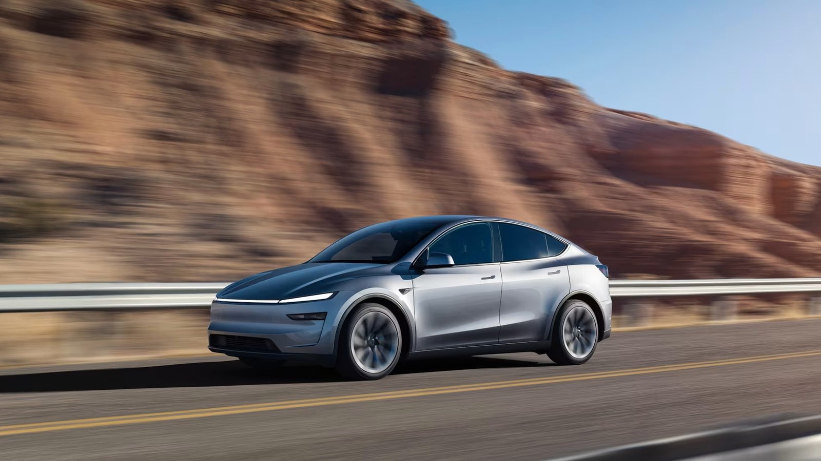 Silver Tesla Model Y Premium driving past red rock cliffs
