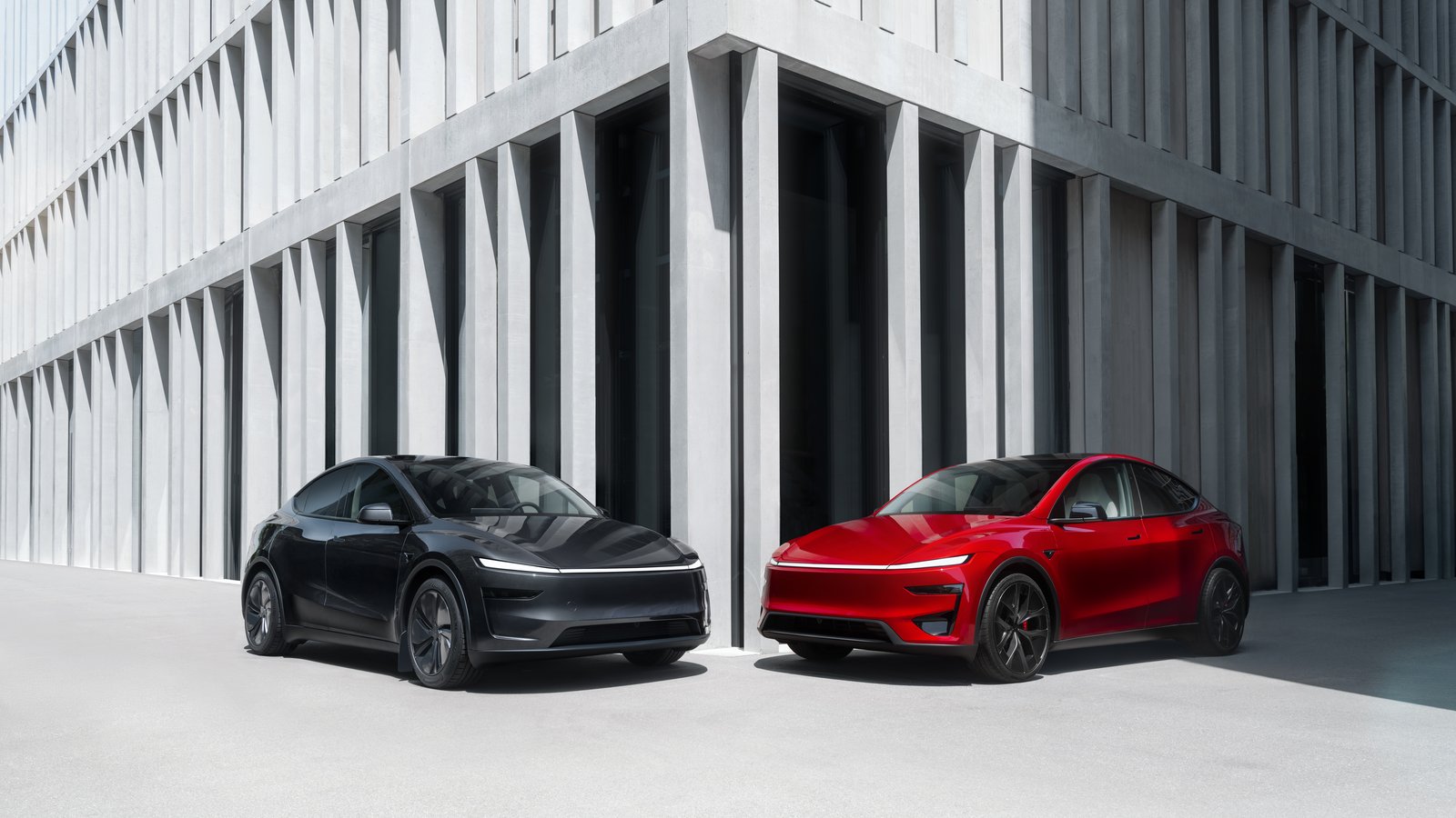 Black and red Tesla Model Y SUVs parked outside a concrete building