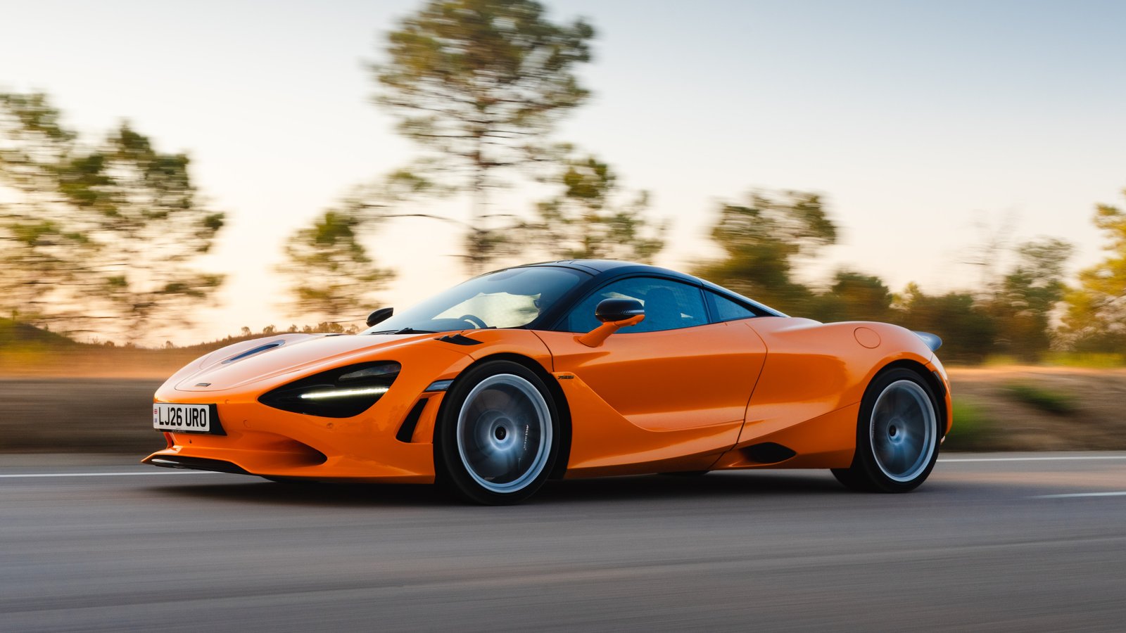 Orange McLaren 750S driving on a road, side profile with motion blur