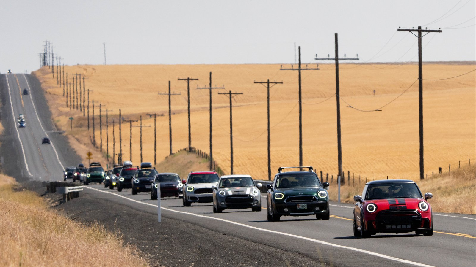 Convoy of MINI cars on a two-lane highway past golden wheat fields