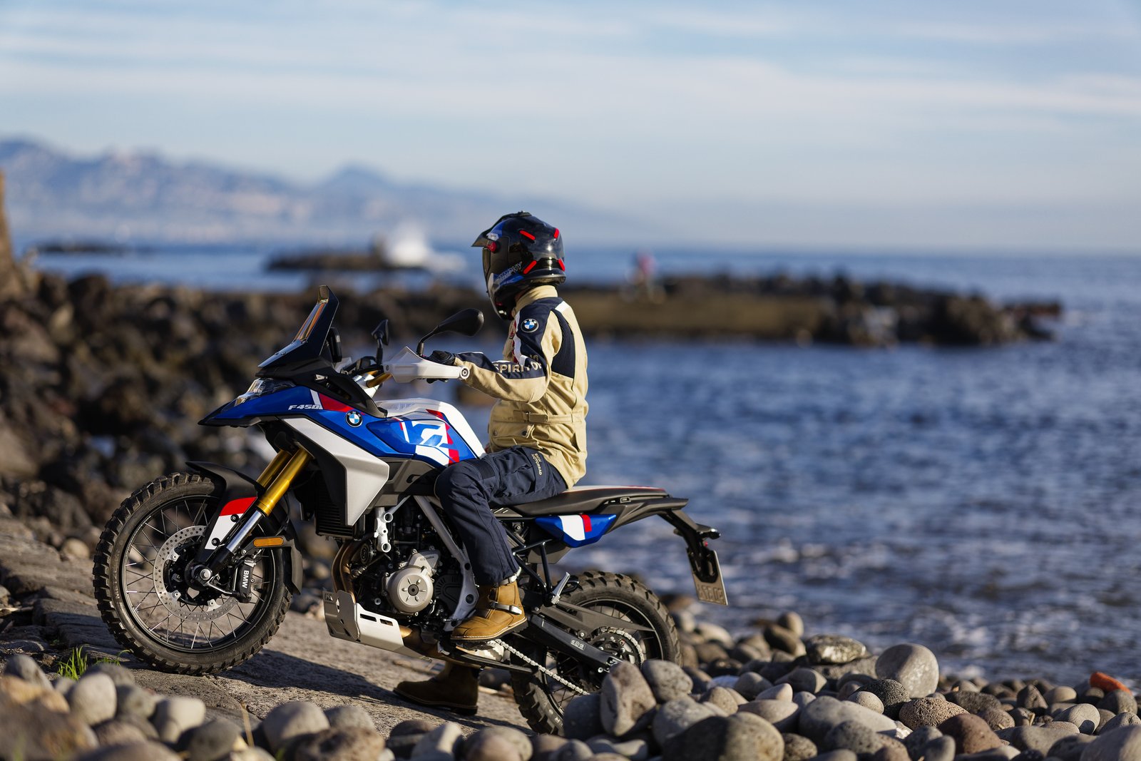Rider seated on a blue-and-white BMW F 450 GS by the sea