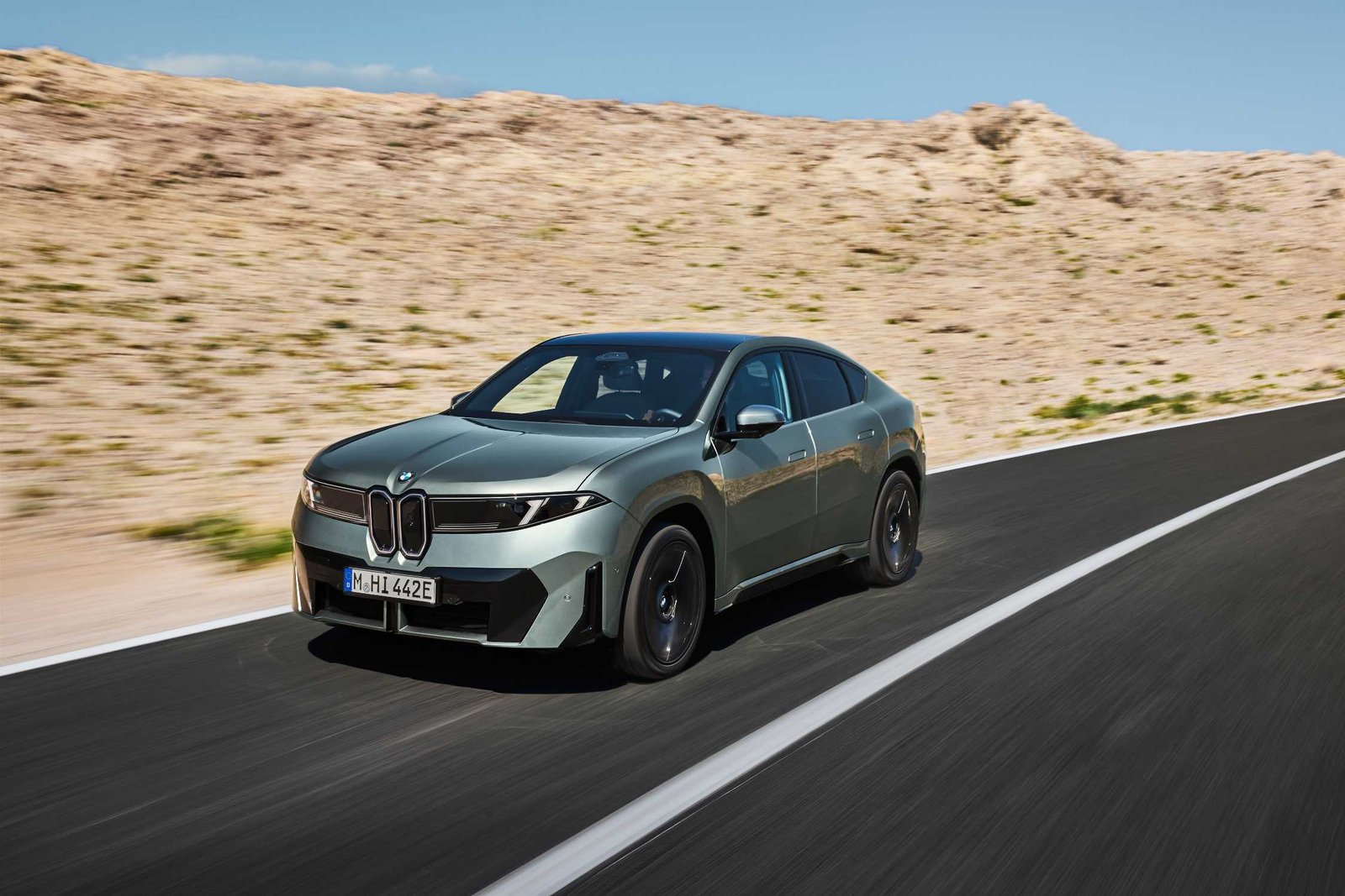 BMW iX4 front three-quarter view driving through a desert landscape