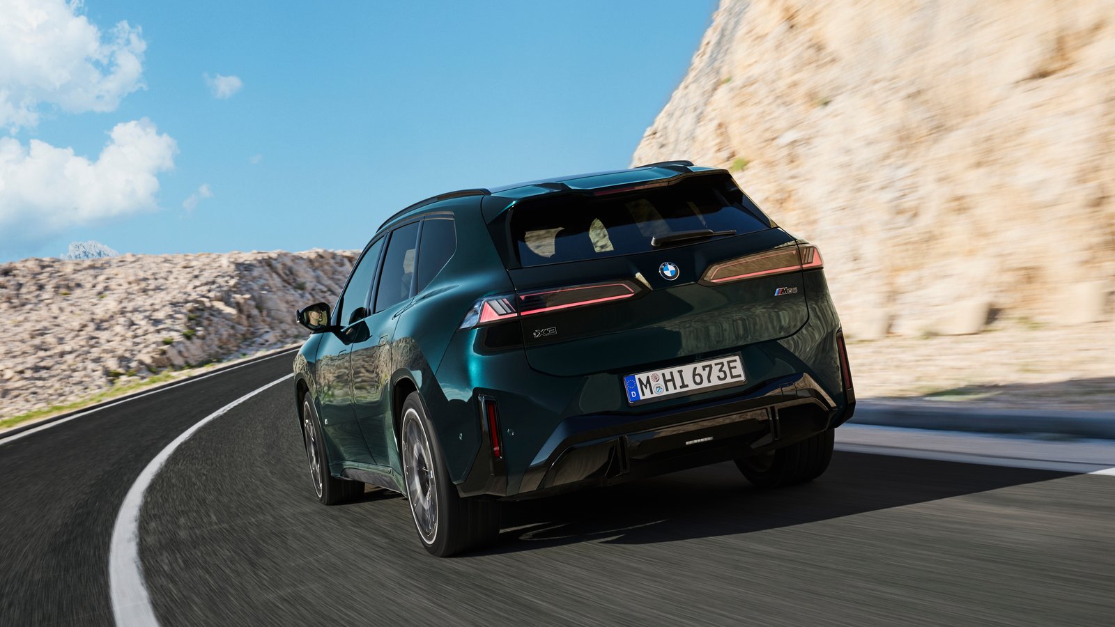 Rear three-quarter view of a dark green BMW iX3 M60 xDrive on a mountain road