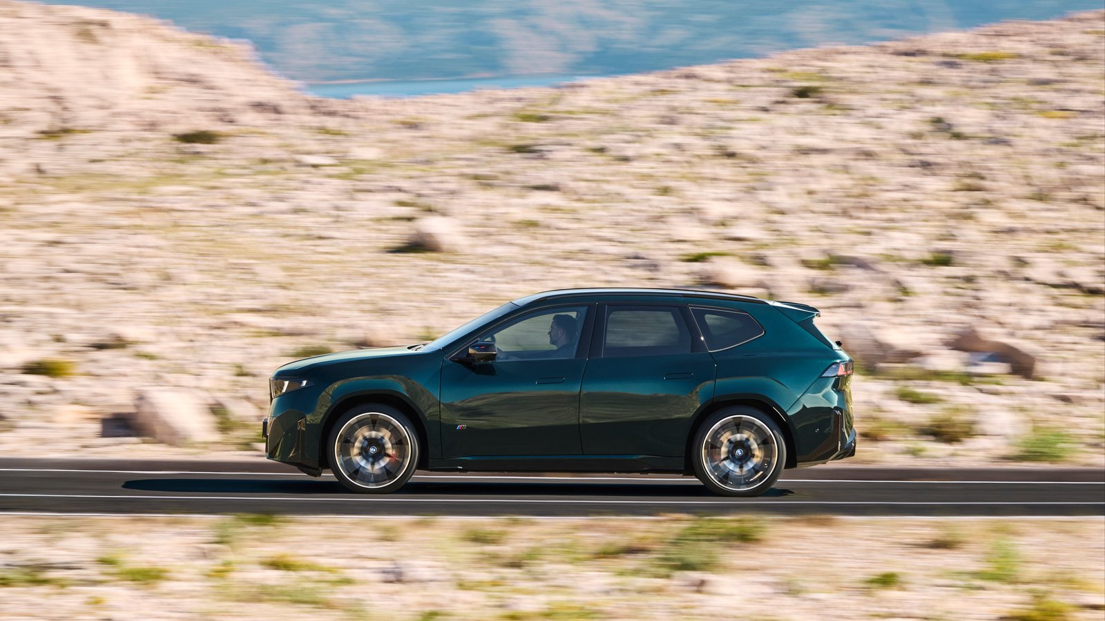 Side profile of a dark green BMW iX3 M60 xDrive in motion