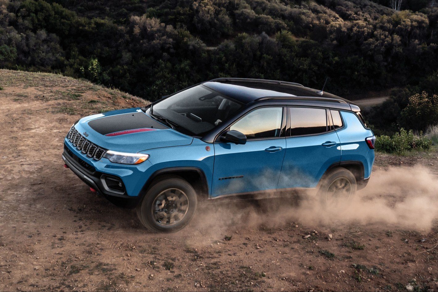 Blue 2027 Jeep Compass Trailhawk kicking up dust on a dirt trail