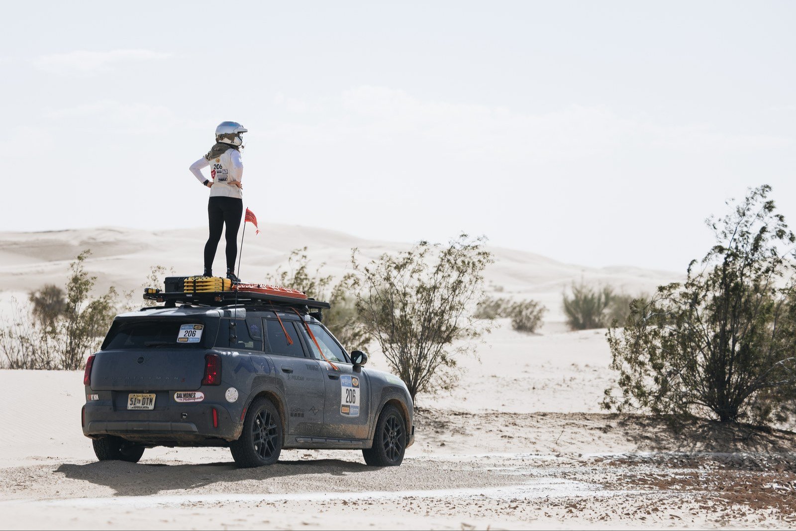 Team member standing on the MINI's roof rack in sand dunes