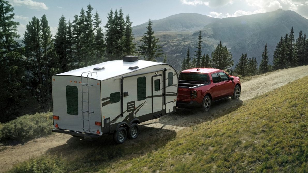 Red Ford Maverick Lariat towing a travel trailer on a mountain road