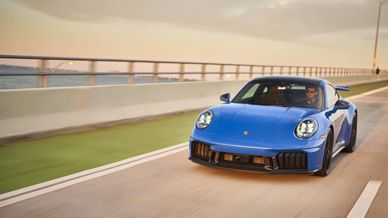 Blue Porsche 911 Carrera GTS T-Hybrid driving across a bridge
