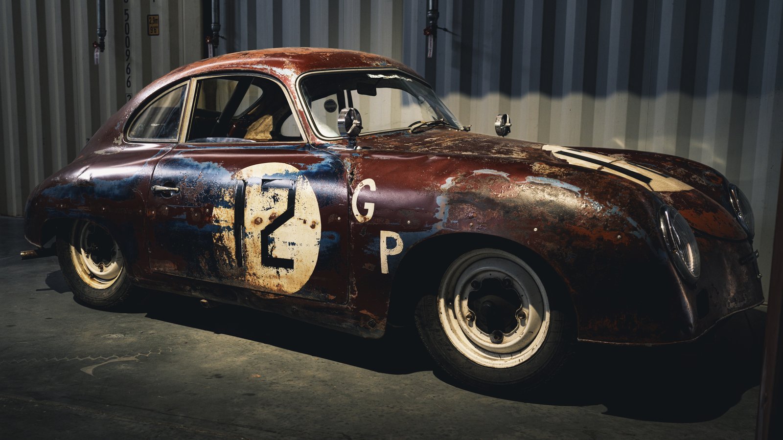 Patina-finished Porsche 356 displayed inside a shipping container