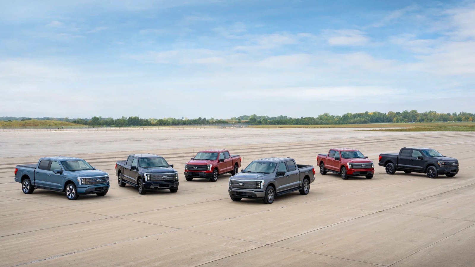 Six Ford F-150 Lightning trucks in different trims and colors on a proving-ground lot