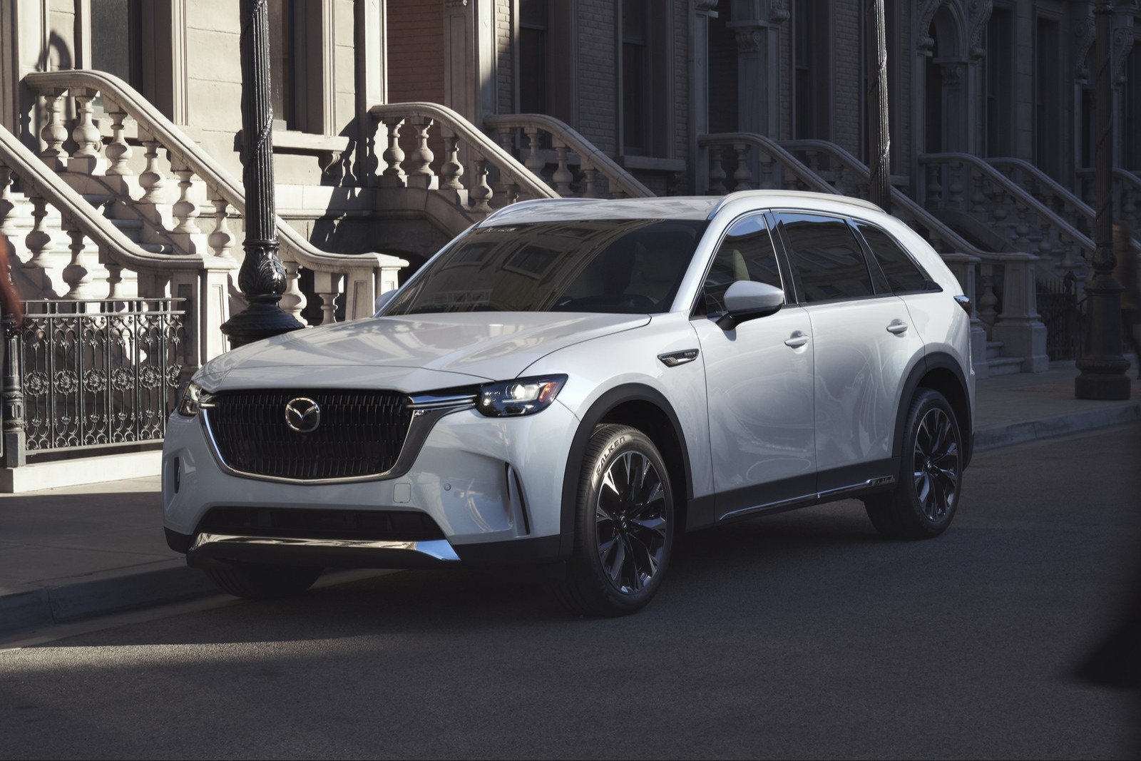 White Mazda CX-90 parked beside brownstone stairs on a city street