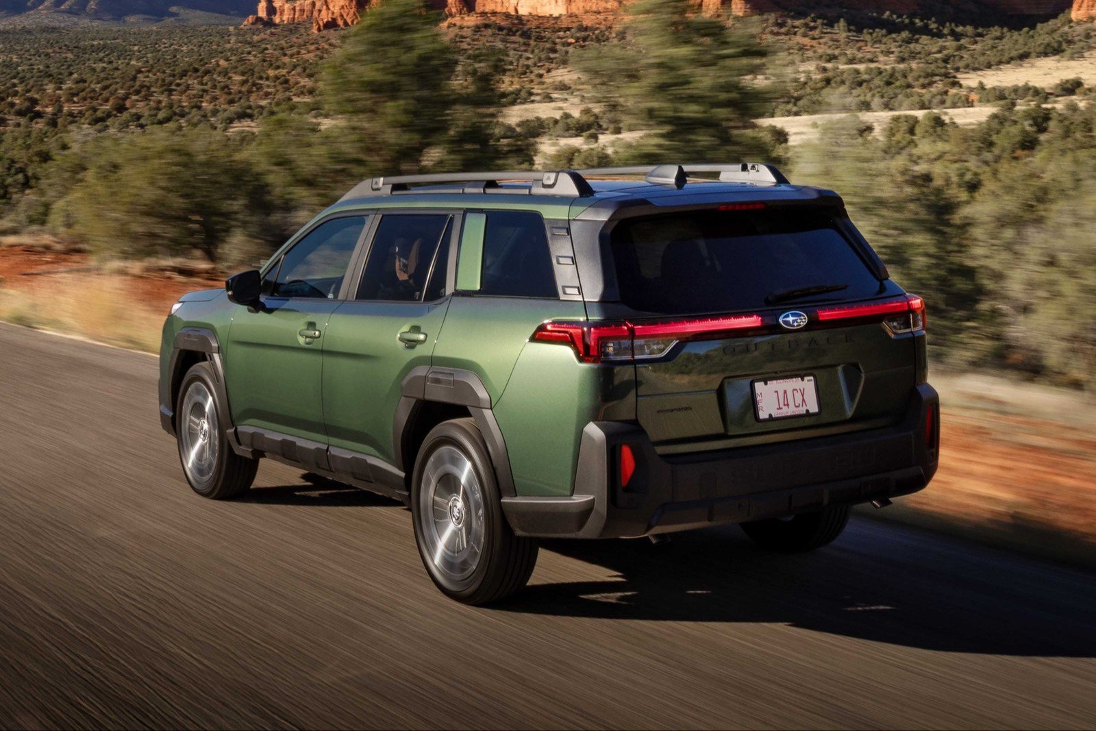 Green Subaru Outback driving on a desert road, rear view