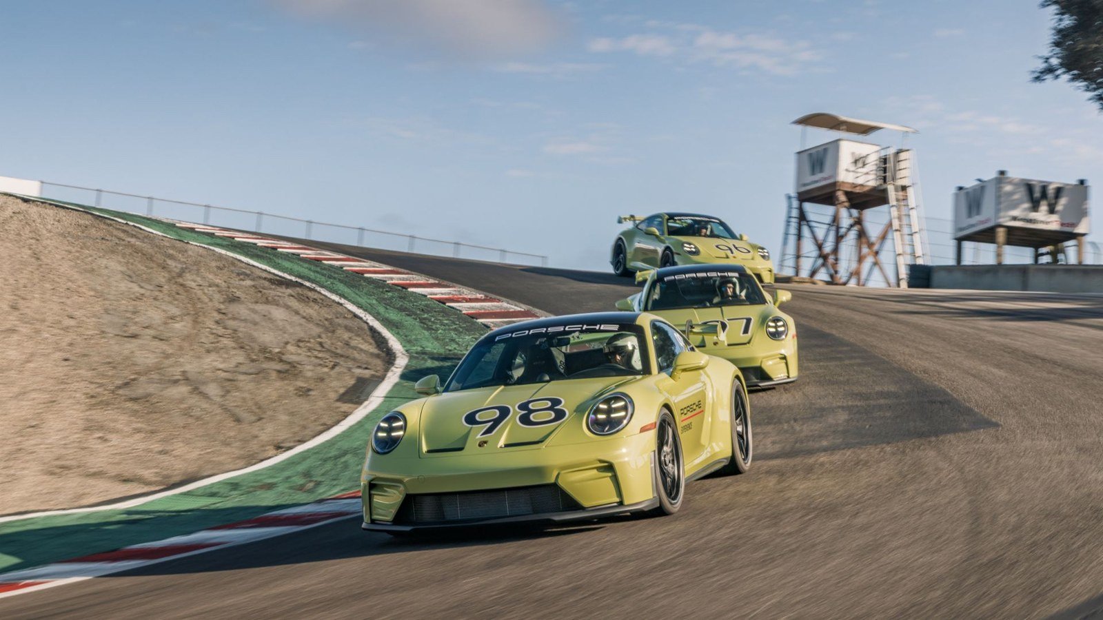 Three yellow Porsche 911 GT3s descending the Corkscrew at Laguna Seca