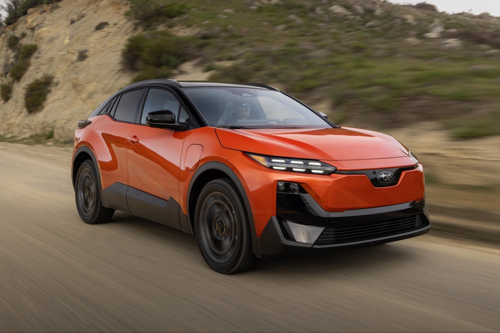 Orange 2027 Subaru Uncharted electric crossover driving on a canyon road