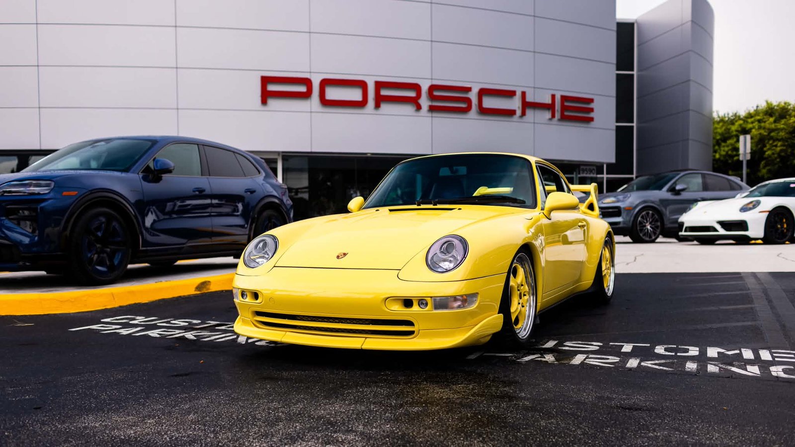 Yellow Porsche 993 with RS-style bodywork parked outside a Porsche dealership
